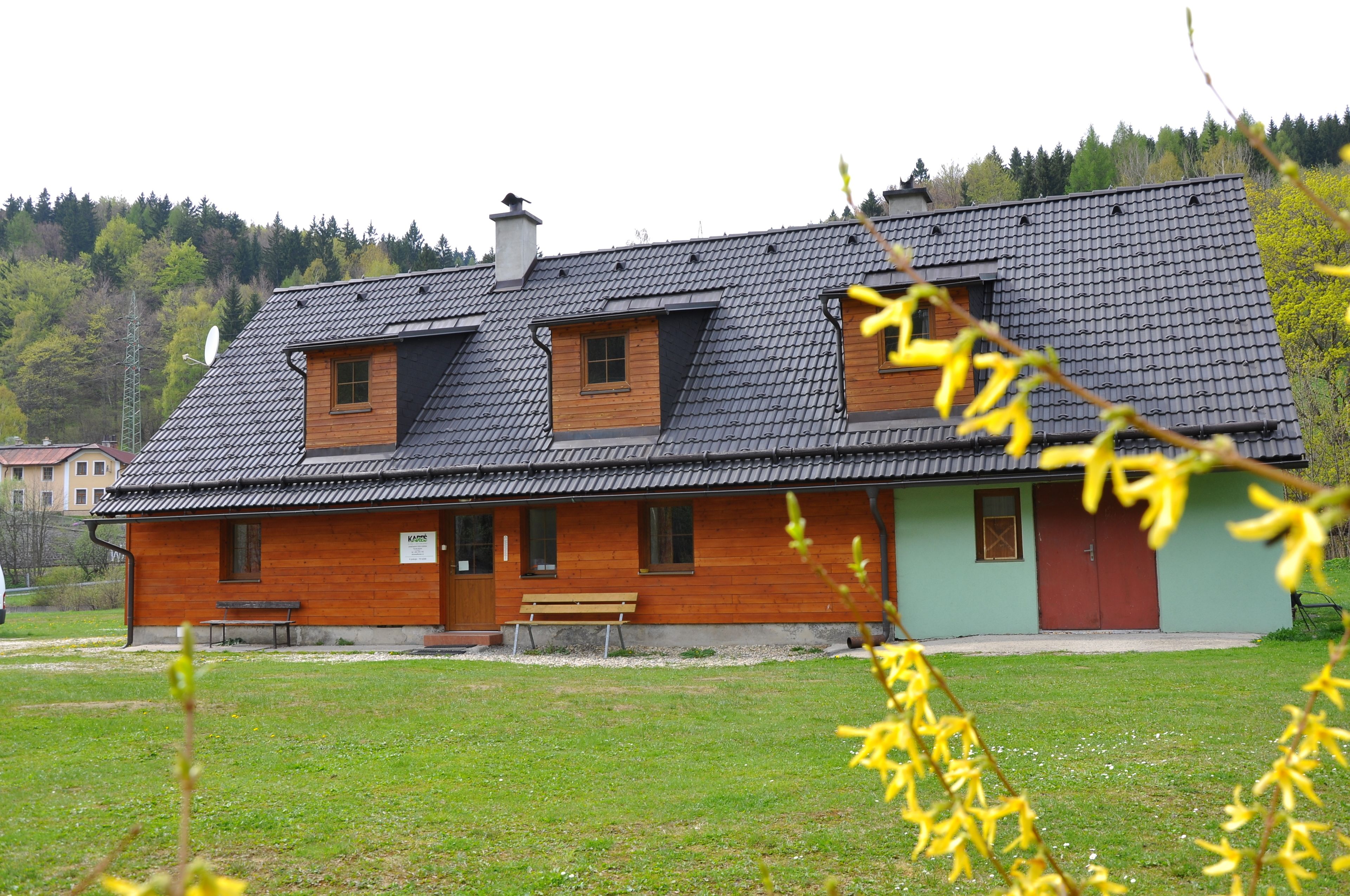 A two-story wooden house with a sloped roof, a front bench, and a red door.