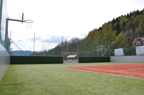 A tennis court with a net, a goal post, and a forested hillside in the background.