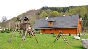 A wooden play structure and a house with a sloped roof in a grassy field. - Chata Pod Vlekem (Loucna nad Desnou)