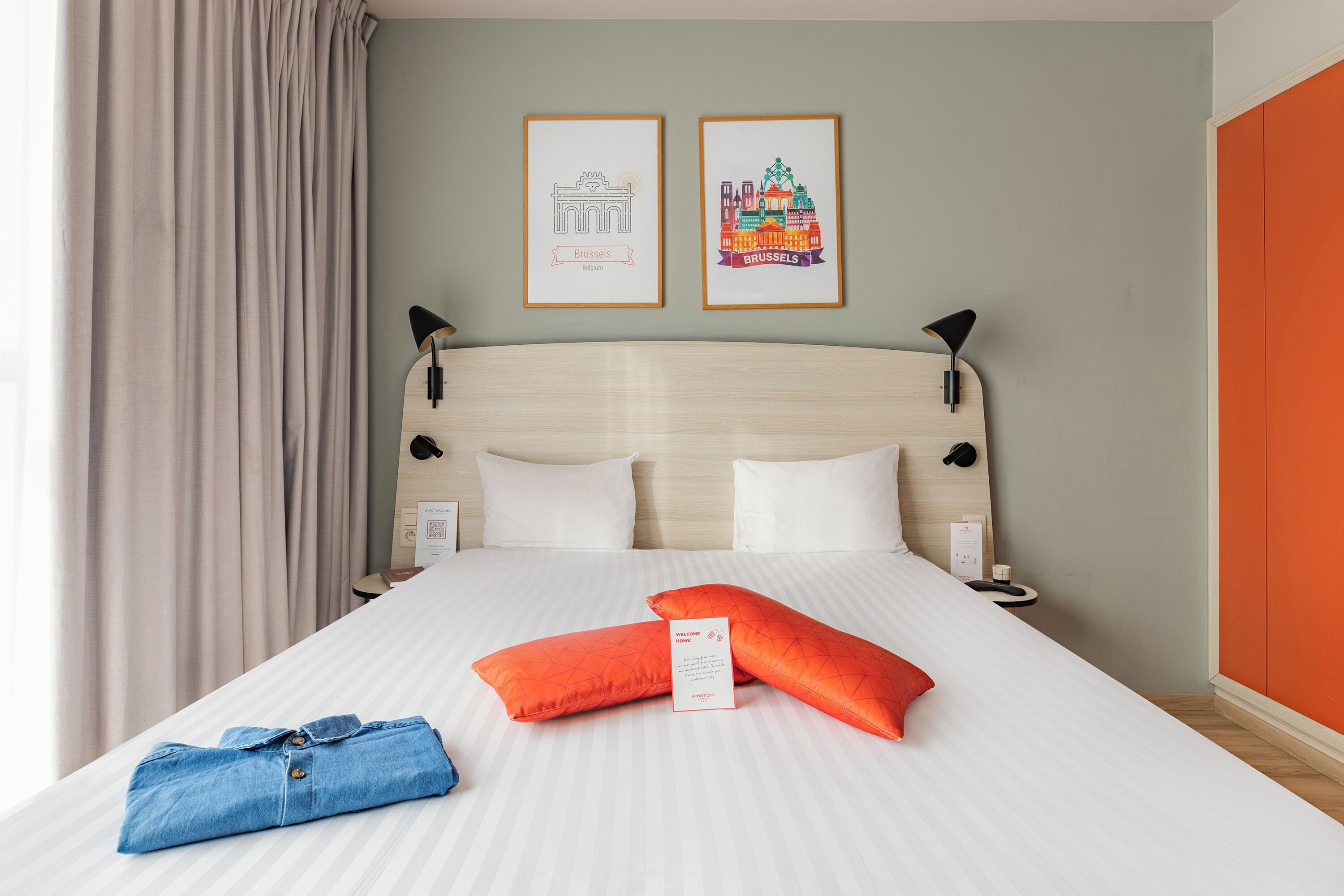 Een net opgemaakt bed met twee kussens, een blauw gevouwen kledingstuk en twee ingelijste foto's aan de muur.