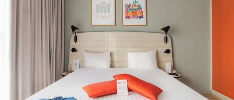 A neatly made bed with two pillows, a folded blue garment, and two framed pictures on the wall.