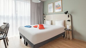 A hotel room with a bed, a desk, a chair, a lamp, and two framed pictures on the wall. - Appart'City Confort Bruxelles Centre Gare du Midi (Brussels)