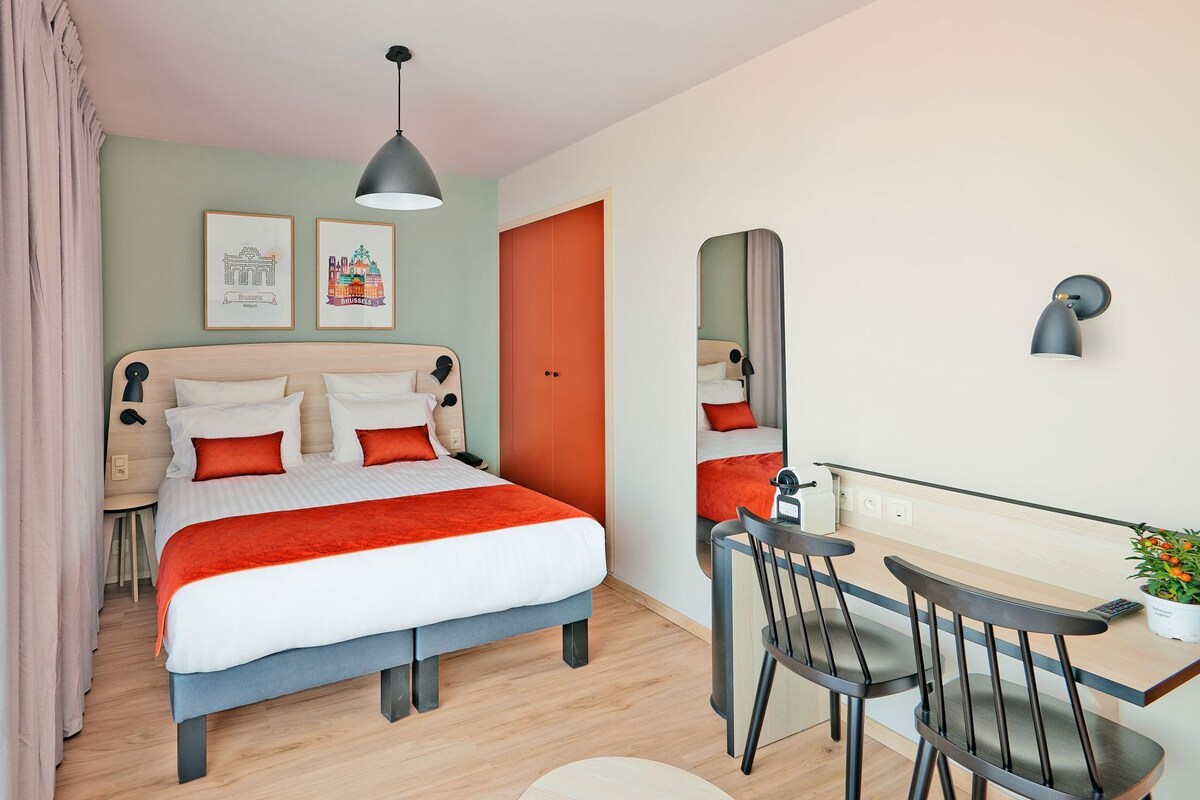 A hotel room with a bed, desk, chair, and a mirror.