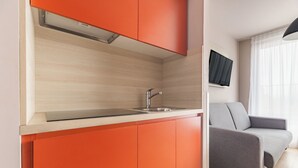A modern kitchen with orange cabinets, a stainless steel sink, and a flat-screen TV mounted on the wall. - Appart'City Confort Bruxelles Centre Gare du Midi (Brussels)