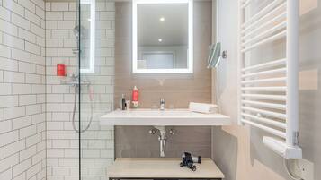 Een moderne badkamer met een douchecabine van glas, een wit wastafelmeubel met een spiegel erboven en een handdoekhouder aan de muur.