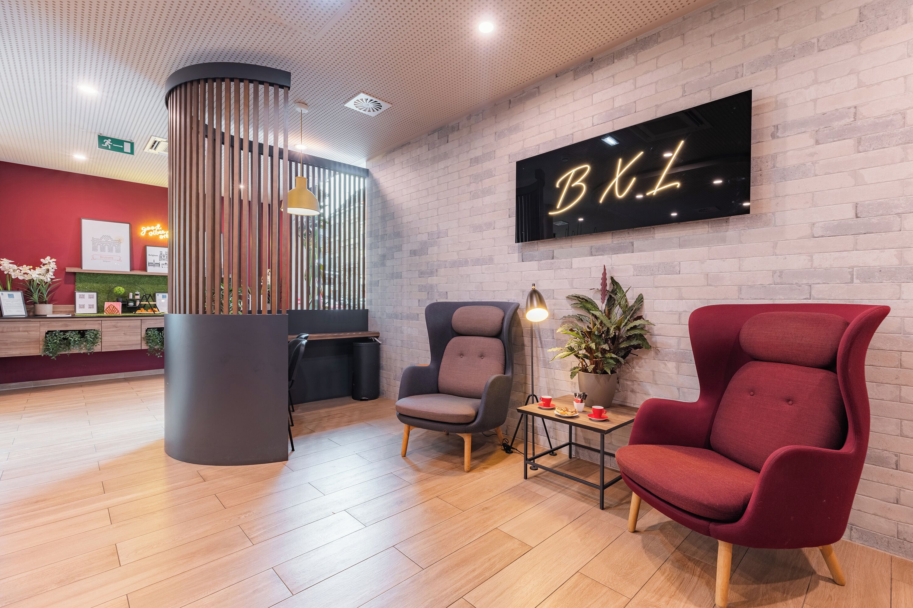 Un espace d’accueil au design moderne, comprenant un comptoir de réception, deux chaises, une plante en pot et un panneau fixé au mur.