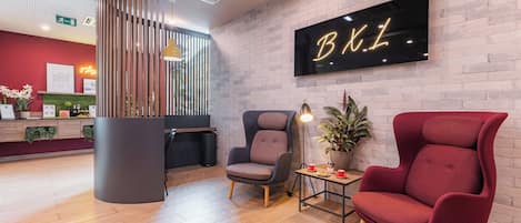A reception area with a modern design, featuring a reception desk, two chairs, a potted plant, and a wall-mounted sign.