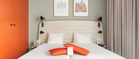 A hotel room with a bed, two framed pictures, a nightstand, a lamp, and a curtain.