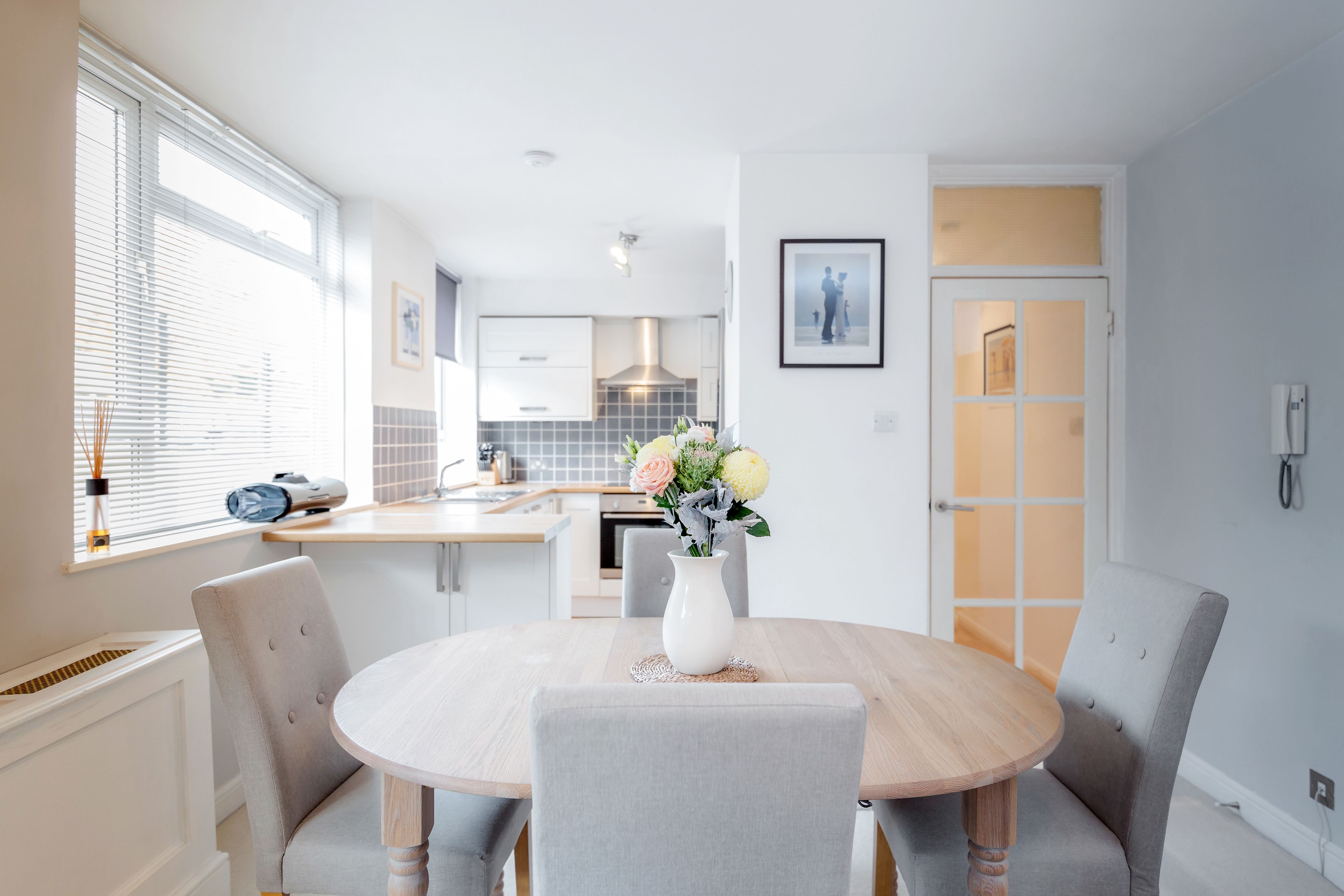 A modern kitchen with white cabinets, a central island, and a dining area with a round table and four chairs.
