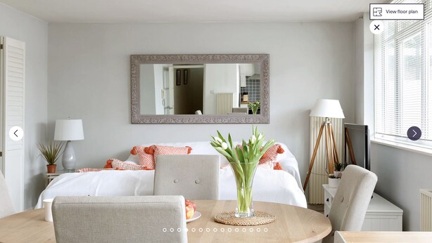 A bedroom with a bed, a bedside table with a lamp, a mirror, and a dining table with chairs. - Putney Court - 1 Bed Apartment by BaseToGo (London)