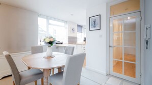 A modern kitchen with a round dining table, grey upholstered chairs, and a vase with flowers. - Putney Court - 1 Bed Apartment by BaseToGo (London)