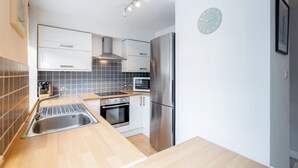 A modern kitchen with white cabinets, a stainless steel refrigerator, a microwave, and a sink. - Putney Court - 1 Bed Apartment by BaseToGo (London)