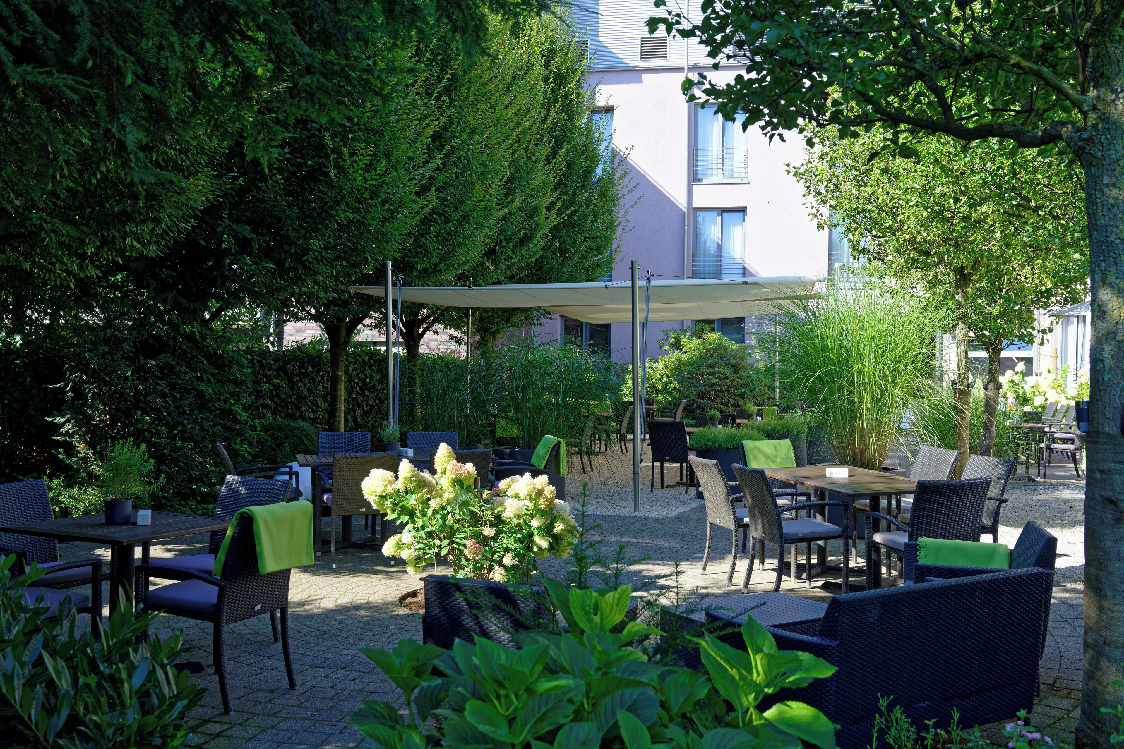 Een terras buiten met tafels en stoelen, omgeven door groen en bomen.