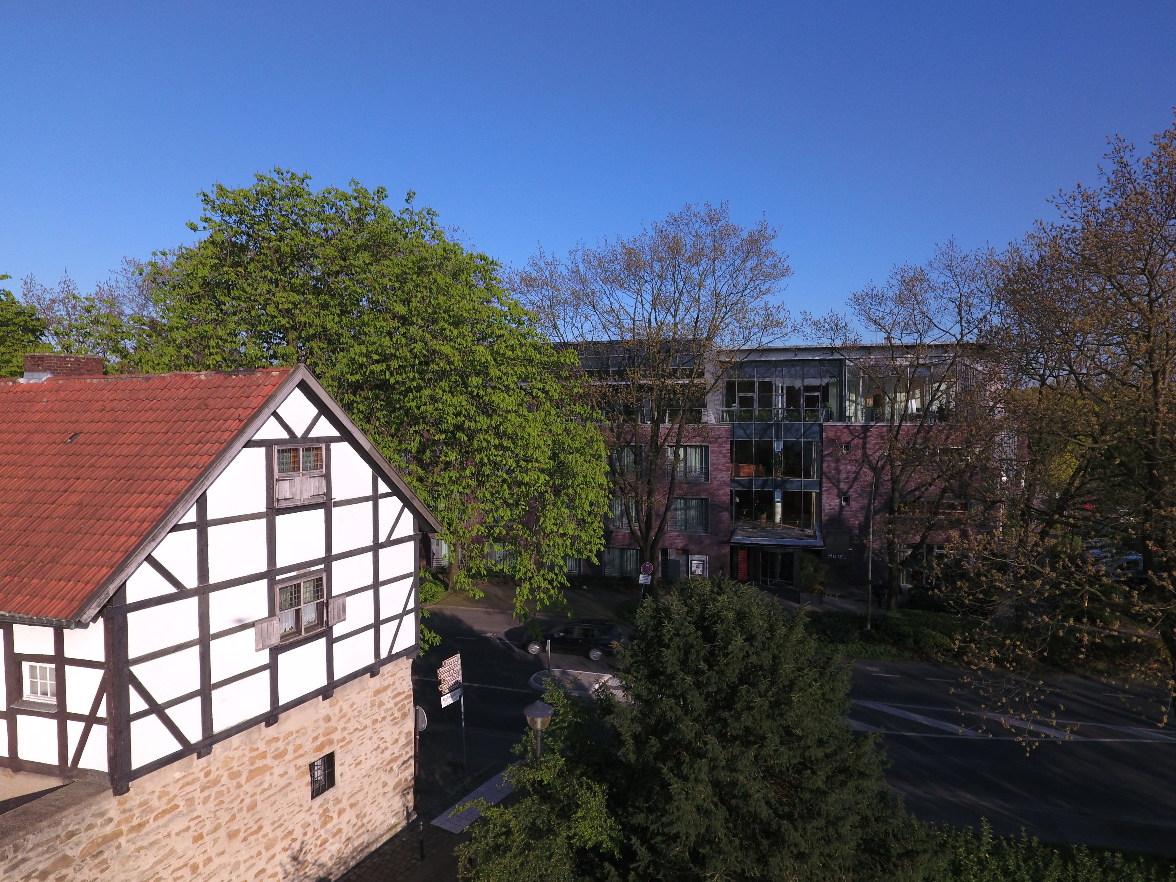 A traditional half-timbered house with a red roof, adjacent to a modern building with a sign indicating a hotel.