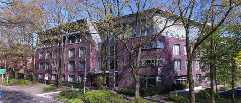 Un hôtel à plusieurs étages, doté d’une façade violette, d’un jardin aménagé et surplombant un ciel d’un bleu limpide.