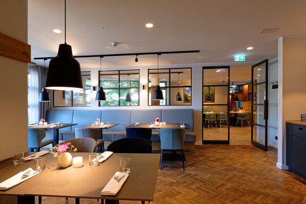 Un restaurante con mesas y cabinas, suelo de madera e iluminación colgante.