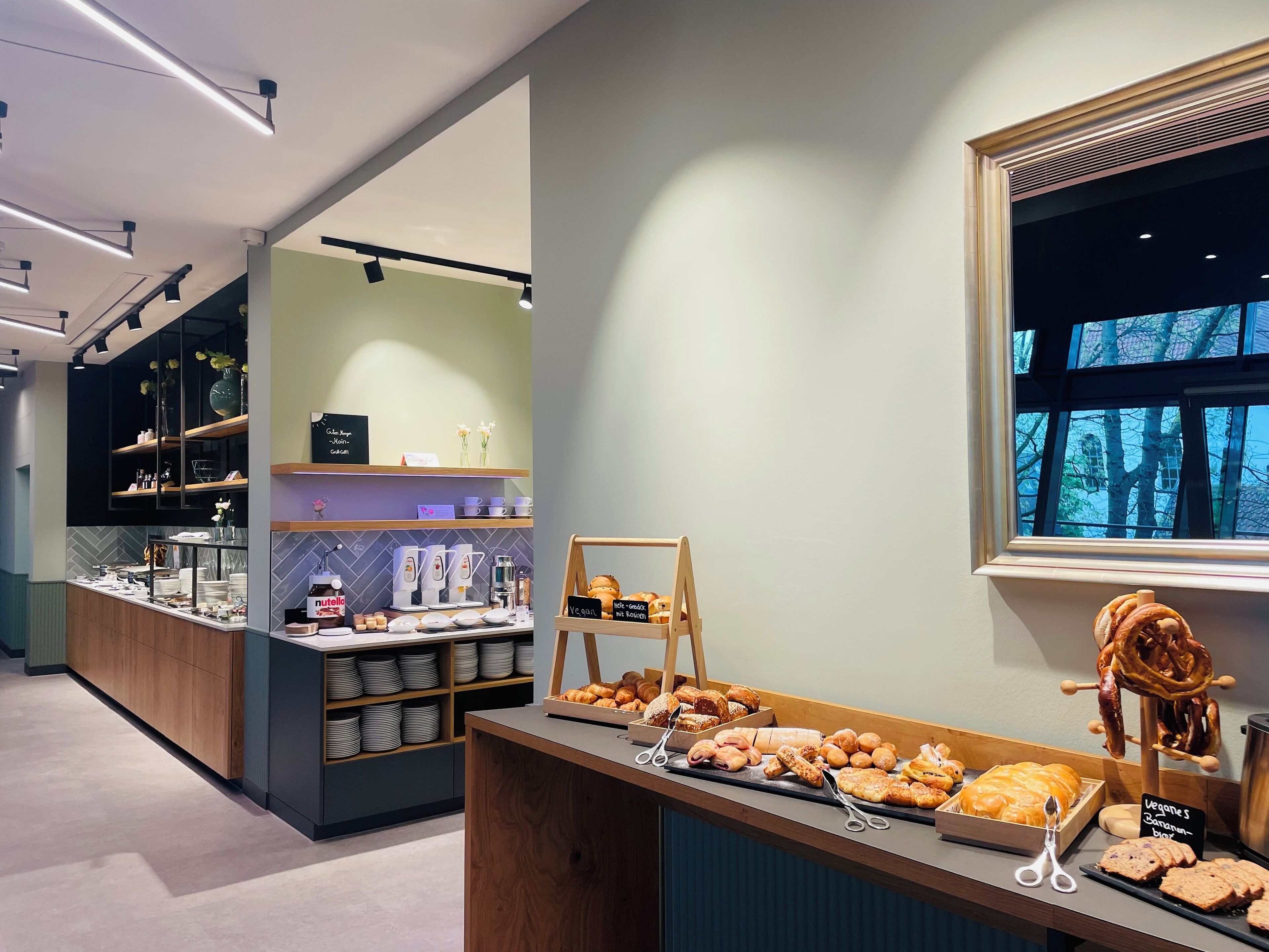 A bakery section with various baked goods displayed on a counter, a coffee station with a coffee machine, and a chalkboard menu.