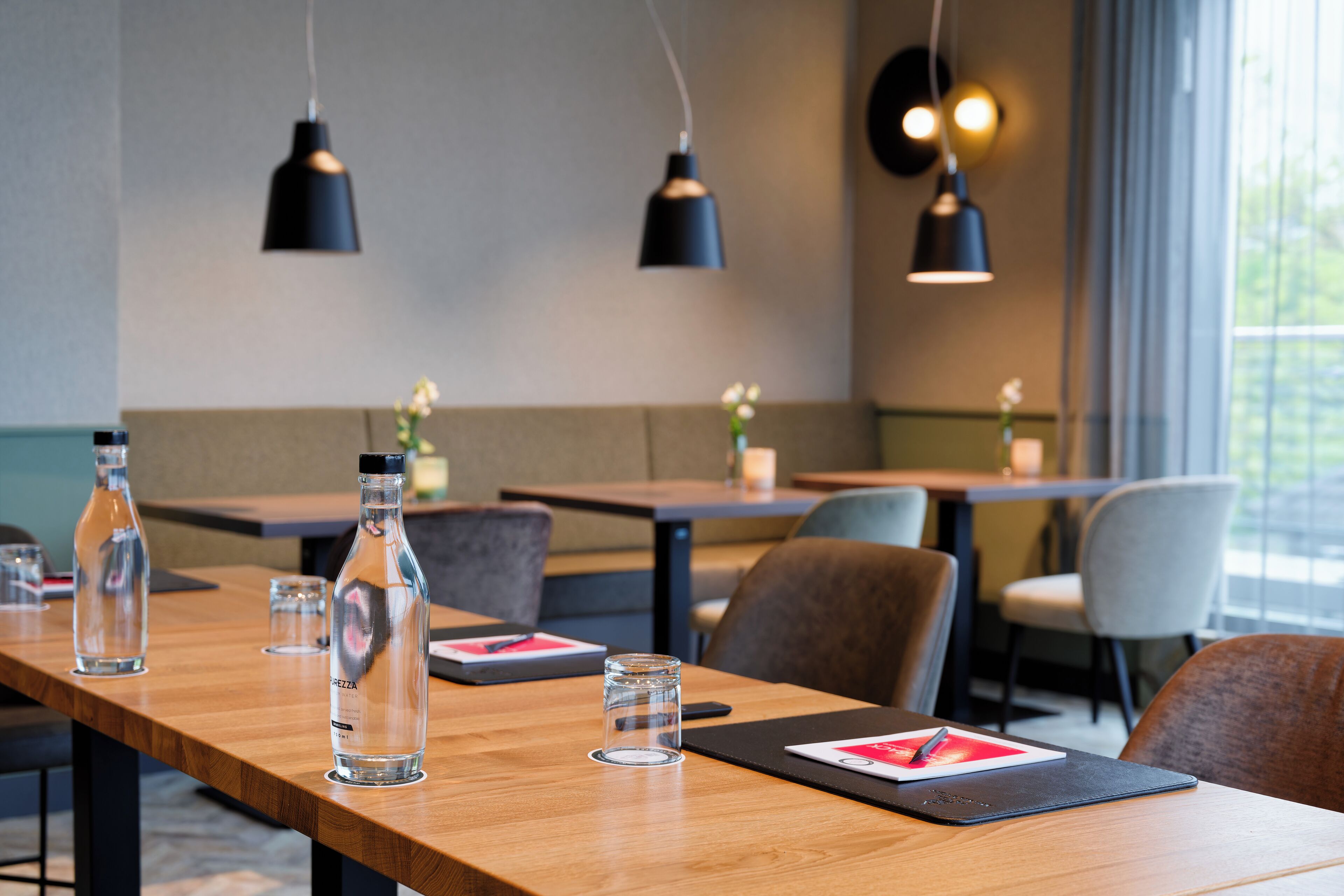 A conference room with a long table, clear glass bottles, and black pendant lights.
