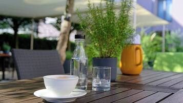 A wooden table with a white cup, a glass of water, a bottle, and a potted plant.