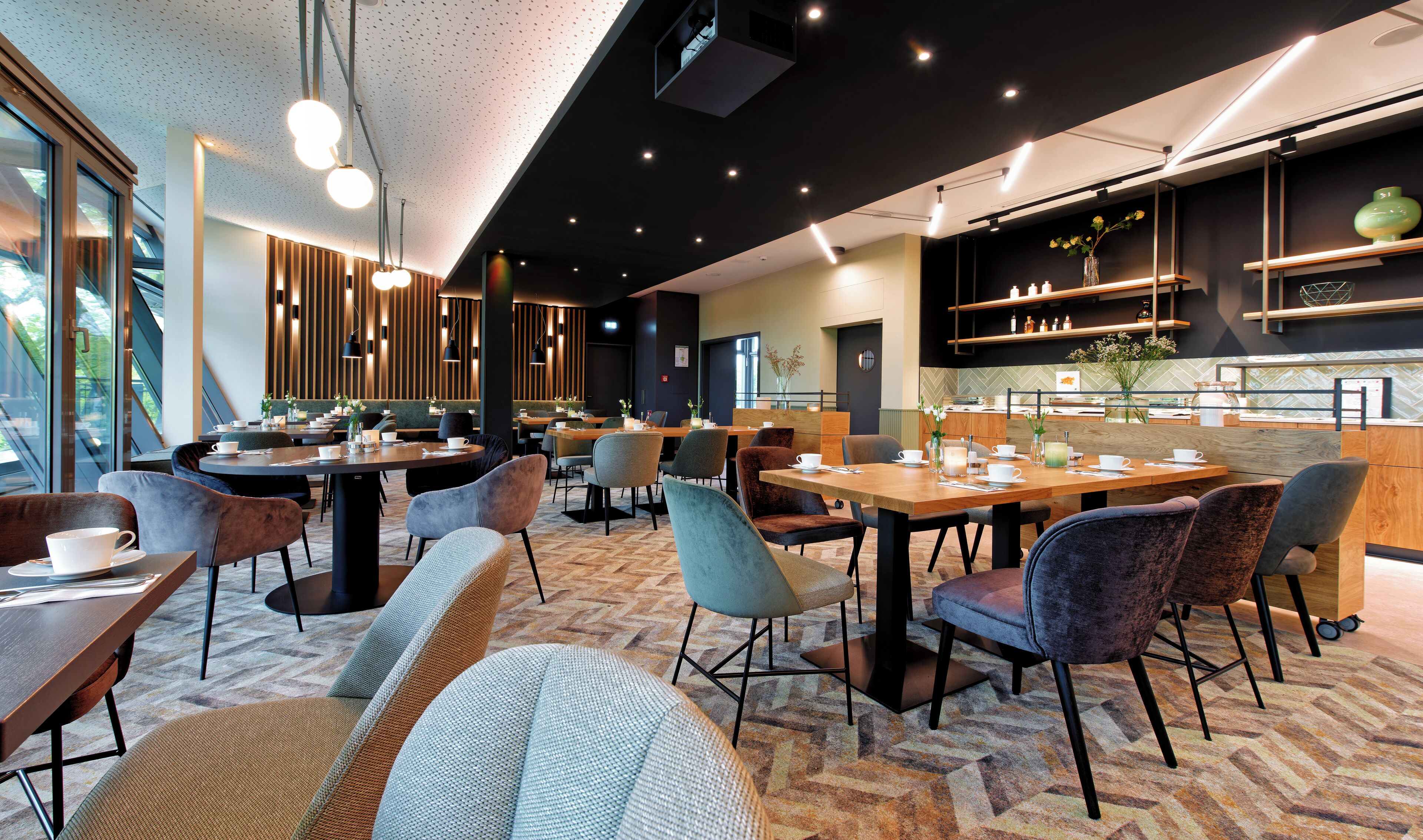 A modern cafe with round tables, cushioned chairs, and a herringbone-patterned carpet.