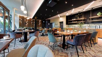 A modern cafe with round tables, cushioned chairs, and a herringbone-patterned carpet.