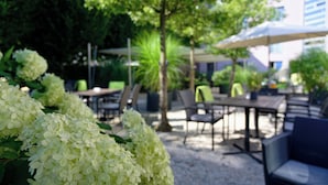 An outdoor seating area with tables and chairs, surrounded by lush greenery and white hydrangea bushes. - Hotel Am Kloster (Werne)
