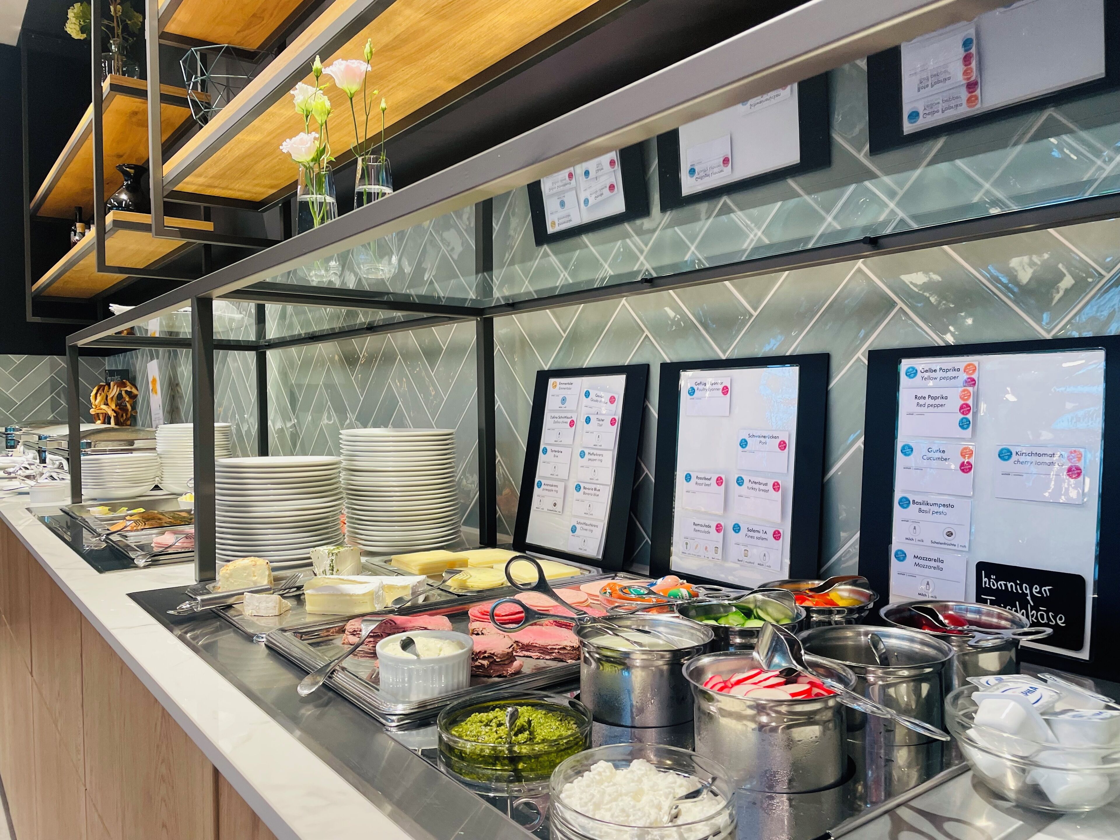 A buffet area with various food options, including meats, cheeses, and salads, displayed on a counter with serving utensils and plates.