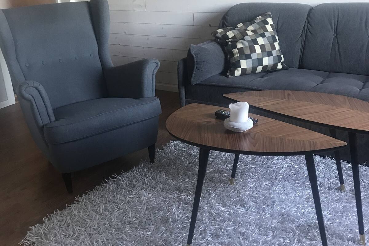 Ein Wohnzimmer mit einem grauen Sessel, einem grauen Sofa, einem runden Couchtisch und einer weißen Tasse.