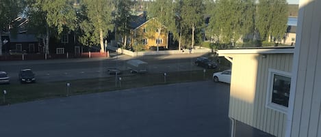 A parking lot with several cars, a white building with a window, and trees in the background.
