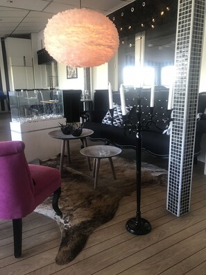 A modern interior with a glass partition, a black sofa with patterned cushions, a pink chair, and a round table with a glass top.