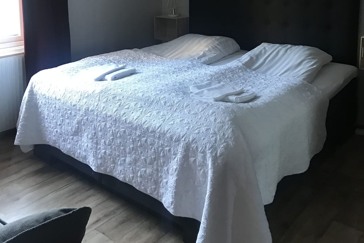 Ein ordentlich bezogenes Bett mit weißen Leinen und Handtüchern, ein dunkles Kopfteil und ein Nachttisch mit Lampe.
