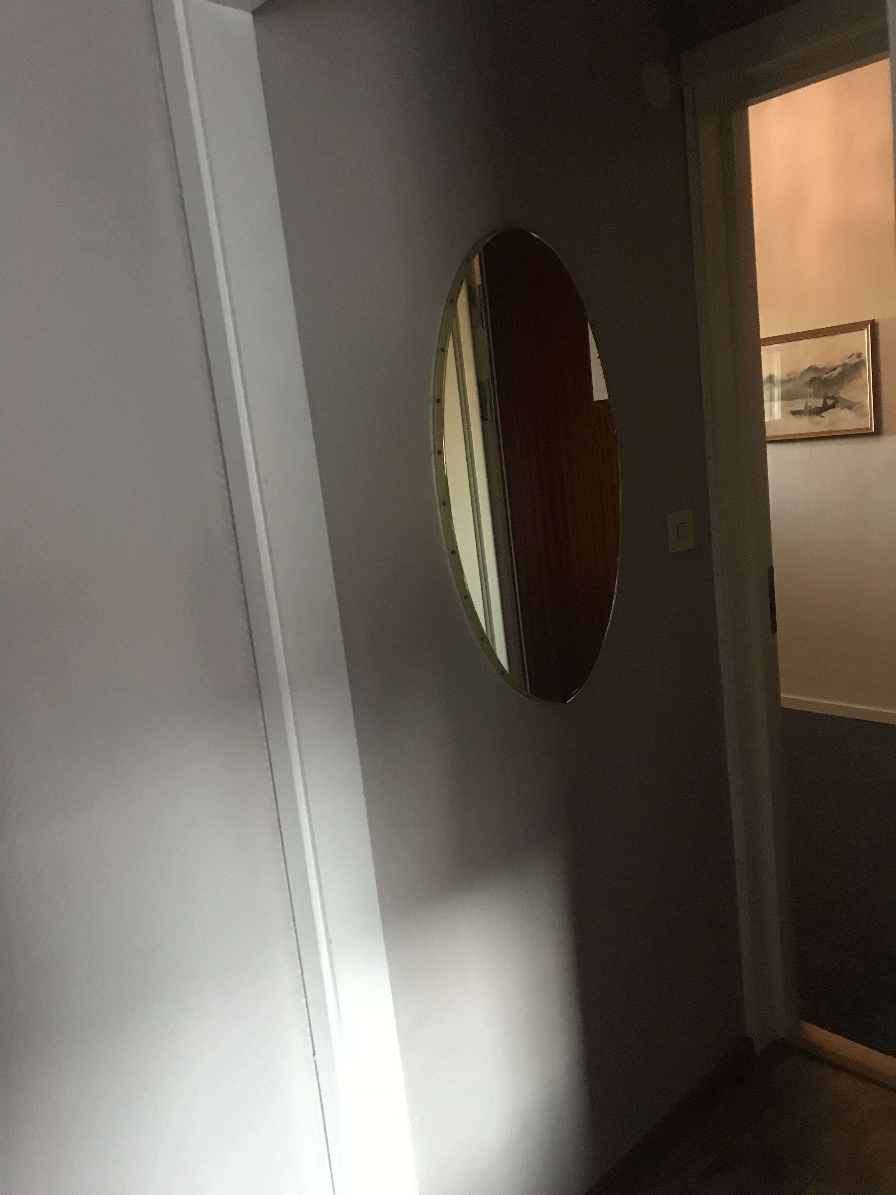 A hallway with a round mirror on the wall, a door, and a framed picture on the adjacent wall.