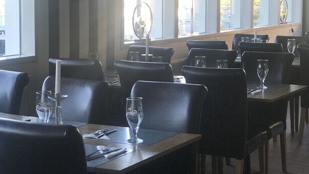 A restaurant with black leather chairs and tables, large windows with striped curtains, and a ceiling with recessed lighting. - Park Hotell (Lycksele)