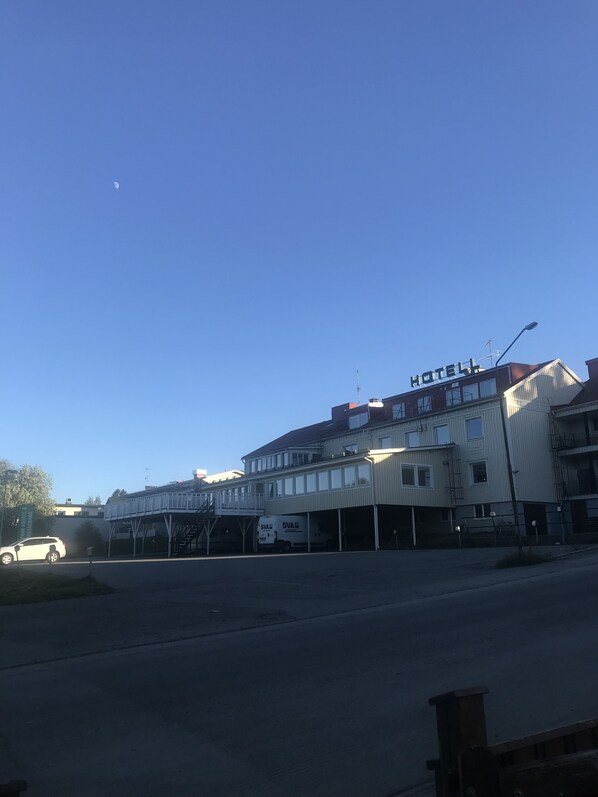 A hotel with a sign reading "HOTEL" on the roof, a van parked in front, and a clear blue sky.