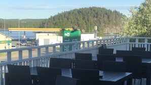 An outdoor deck with tables and chairs, overlooking a road with vehicles and a gas station in the background. - Park Hotell (Lycksele)
