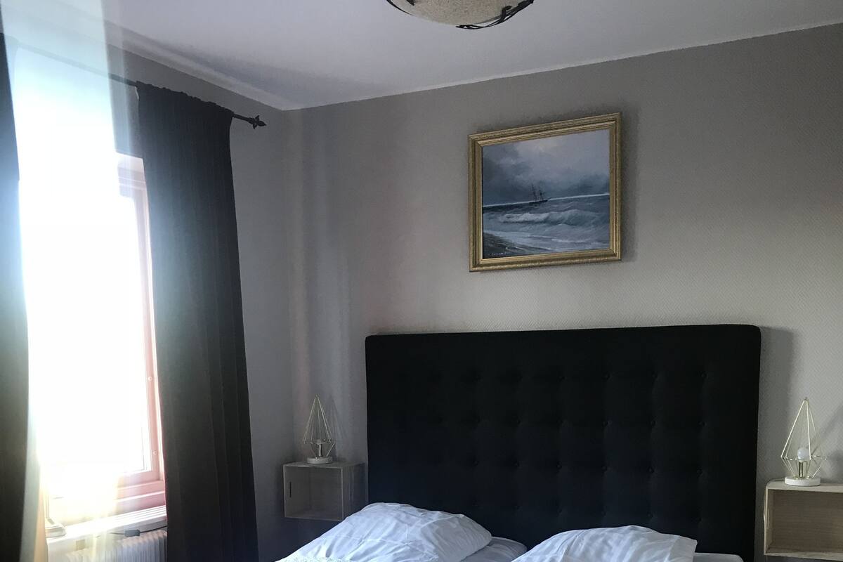 Ein ordentlich bezogenes Bett mit weißen Bettwäsche, einem dunklen Kopfteil und einem gerahmten Gemälde darüber.