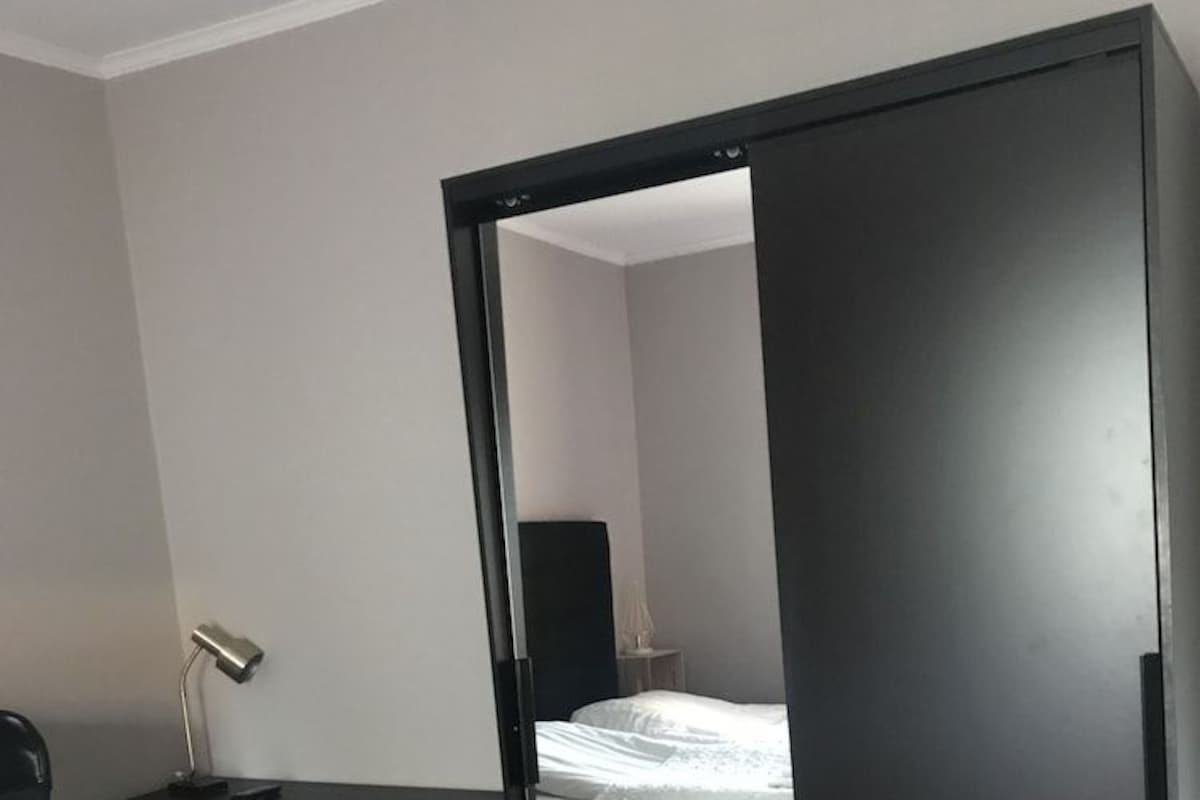 A room with a bed, a desk with a chair, a lamp, and a wardrobe.