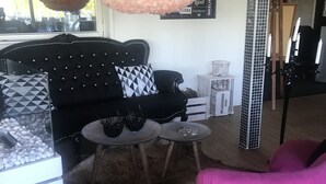 A modern living room with a black tufted sofa, a pink armchair, a round coffee table, and a fluffy white pendant light. - Park Hotell (Lycksele)