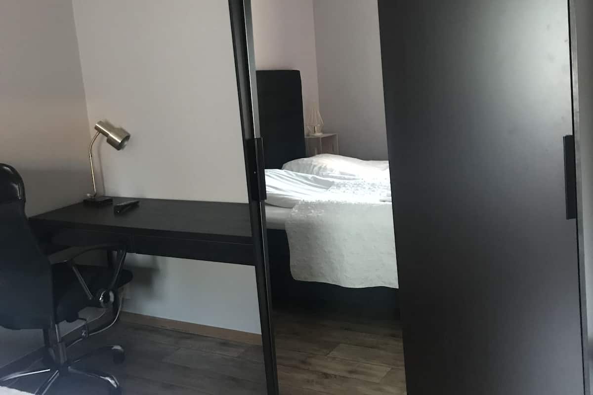 A room with a desk, chair, bed, and a wardrobe.