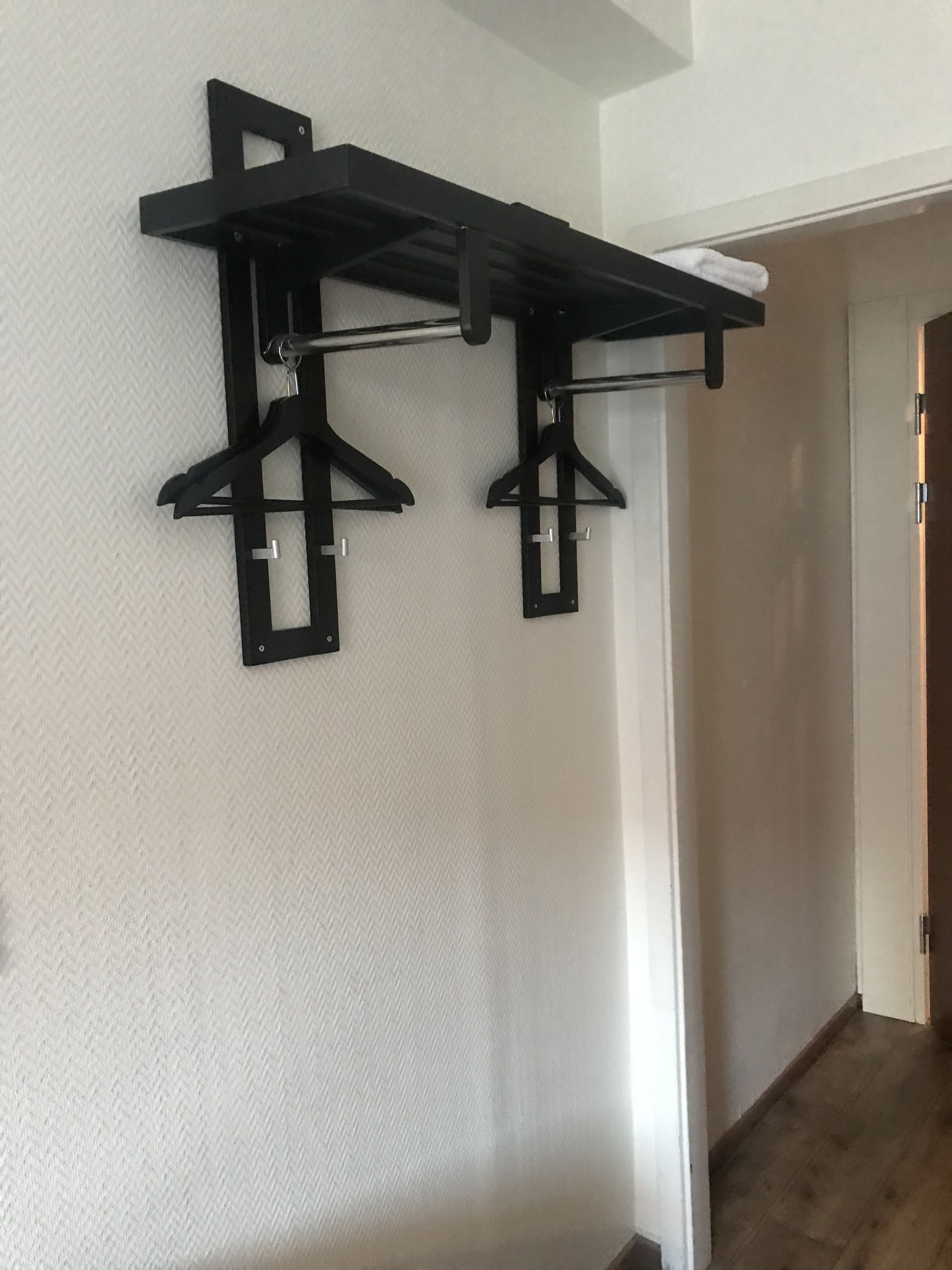 Un pasillo con un perchero de metal negro fijado a la pared, sosteniendo dos colgadores negros.
