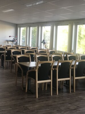 A conference room with multiple tables and chairs, large windows with curtains, and a ceiling with recessed lighting.