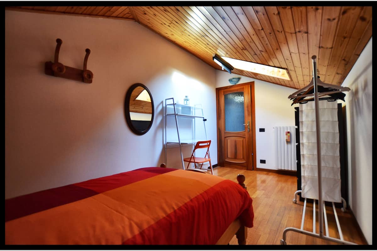 A bedroom with a bed, a chair, a radiator, a mirror, and a coat rack.