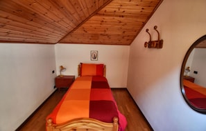 Ein Zimmer mit einem Einzelbett, Holzboden, einem Nachttisch mit Lampe und einem an der Wand befestigten Spiegel.