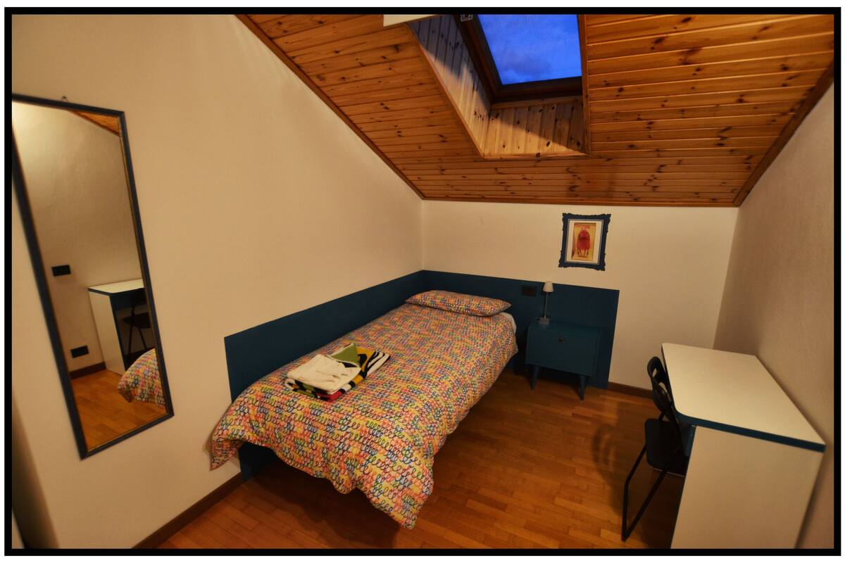 A small bedroom with a single bed, a desk, a chair, and a skylight.