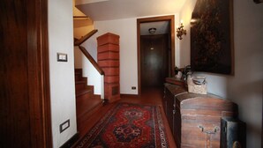 A hallway with a wooden staircase, a red carpet, and a vintage sewing machine on a cabinet. - B&B Luisa (Bergamo)