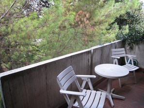 An outdoor patio with a round table and two white chairs, surrounded by a concrete wall and dense foliage. - B&B Luisa (Bergamo)