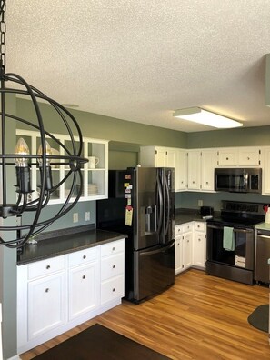 A modern kitchen with white cabinets, stainless steel appliances, and a wooden floor. - Tailslide Inn 4 Bedroom Home by RedAwning (Supply)