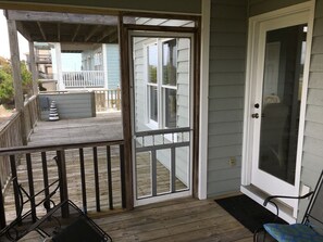 A wooden deck with a railing, a door with a screen, and a chair.