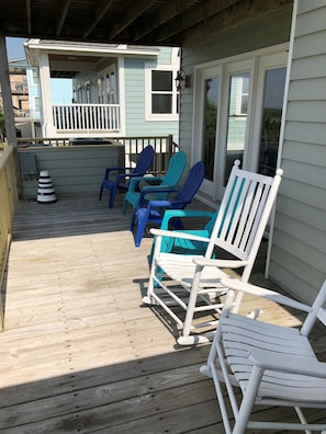 A wooden deck with outdoor seating, including white and blue chairs, and a building with a balcony.