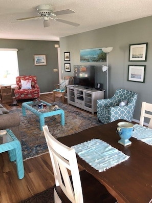A living room with a dining table, chairs, a television, and a ceiling fan.